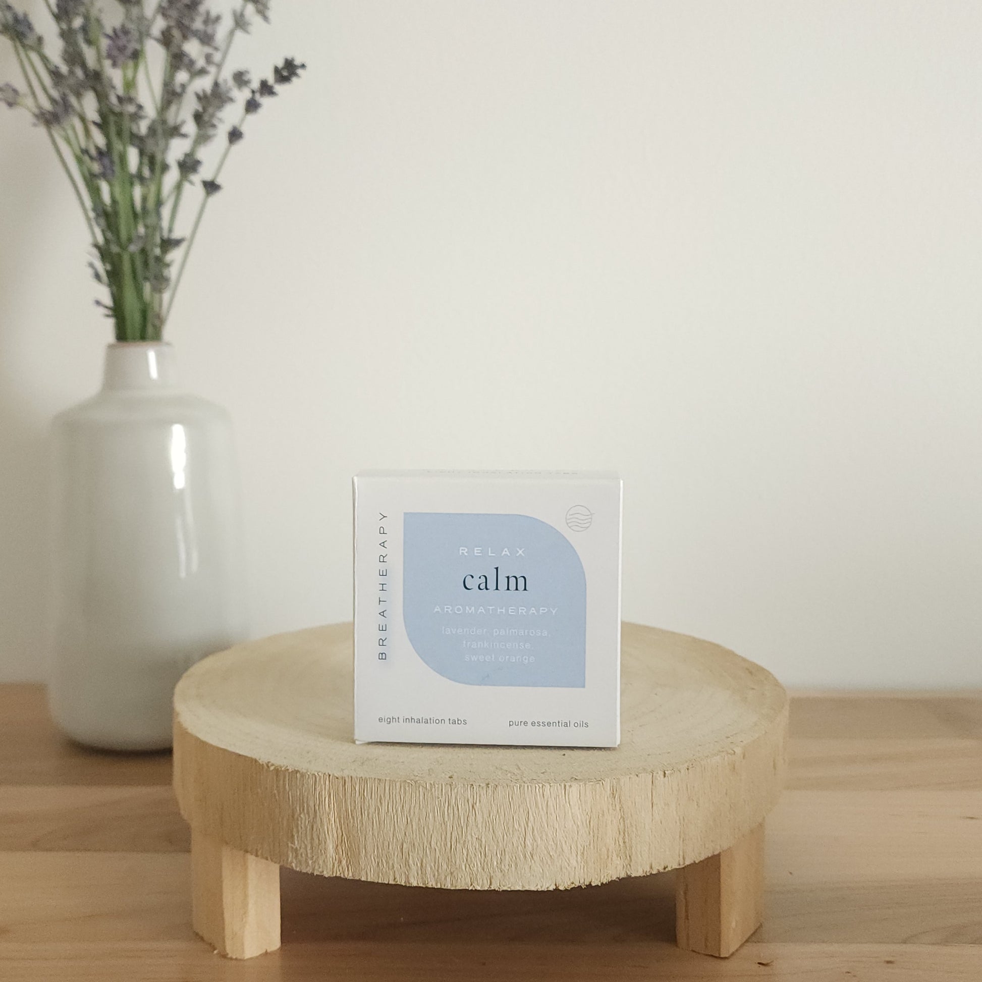 RELAX calm aromatherapy patches package with light blue label displayed on a round wooden stand next to a white ceramic vase with dried lavender stems