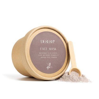 Round kraft paper container labeled 'DESESH FACE MASK' with ingredients listed, next to a small wooden scoop and a pile of gray powder on a white background.