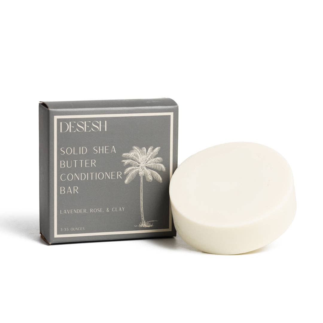 Gray box labeled 'DESESH SOLID SHEA BUTTER CONDITIONER BAR LAVENDER ROSE & CLAY' with a palm tree illustration, next to a round, white solid shea butter conditioner bar on a white background.