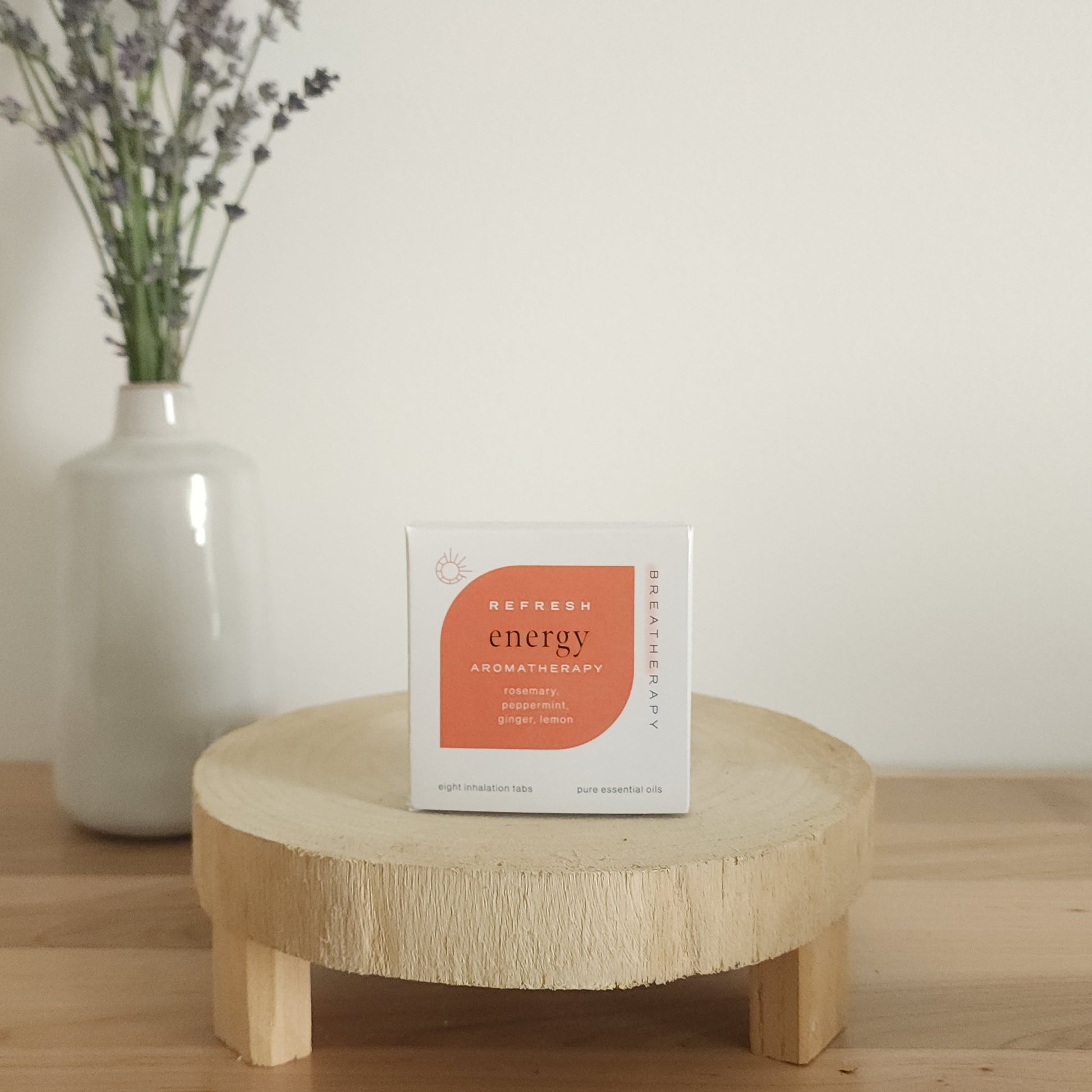 REFRESH energy breathe aromatherapy patches package with orange label displayed on a round wooden stand next to a white ceramic vase with dried lavender stems