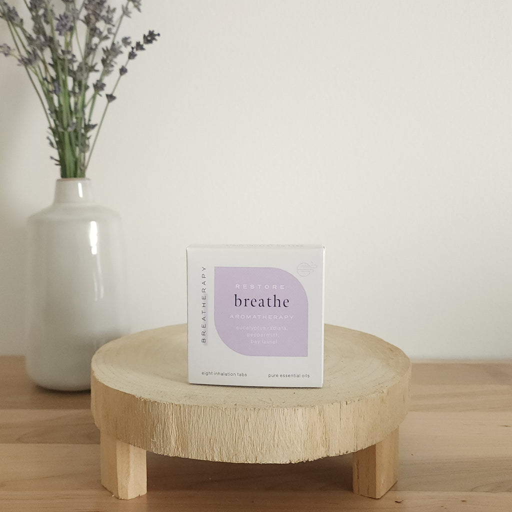 RESTORE breathe aromatherapy patches package with purple label displayed on a round wooden stand next to a white ceramic vase with dried lavender stems
