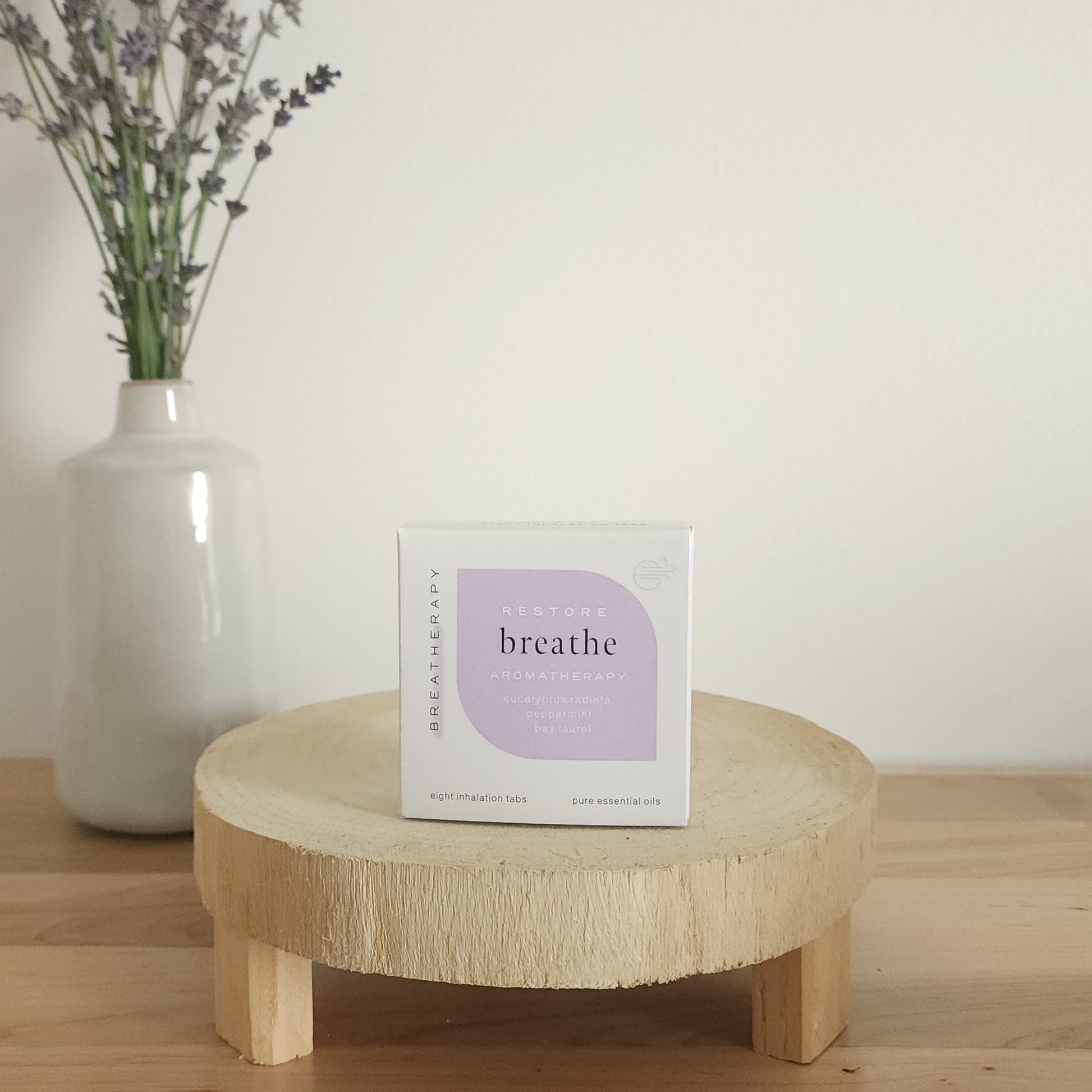 RESTORE breathe aromatherapy patches package with purple label displayed on a round wooden stand next to a white ceramic vase with dried lavender stems
