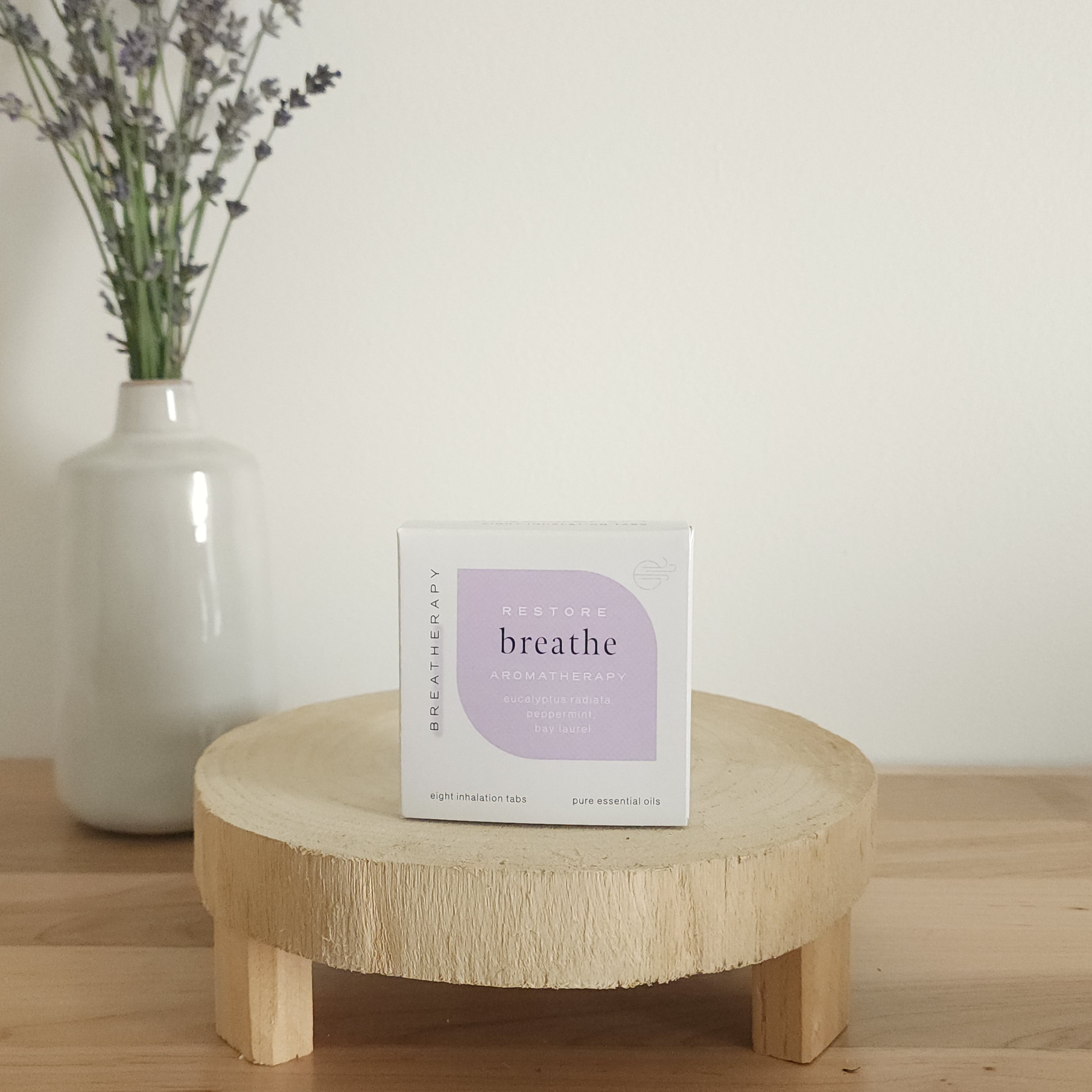 RESTORE breathe aromatherapy patches package with purple label displayed on a round wooden stand next to a white ceramic vase with dried lavender stems