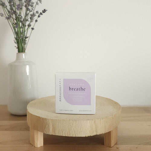 RESTORE breathe aromatherapy patches package with purple label displayed on a round wooden stand next to a white ceramic vase with dried lavender stems