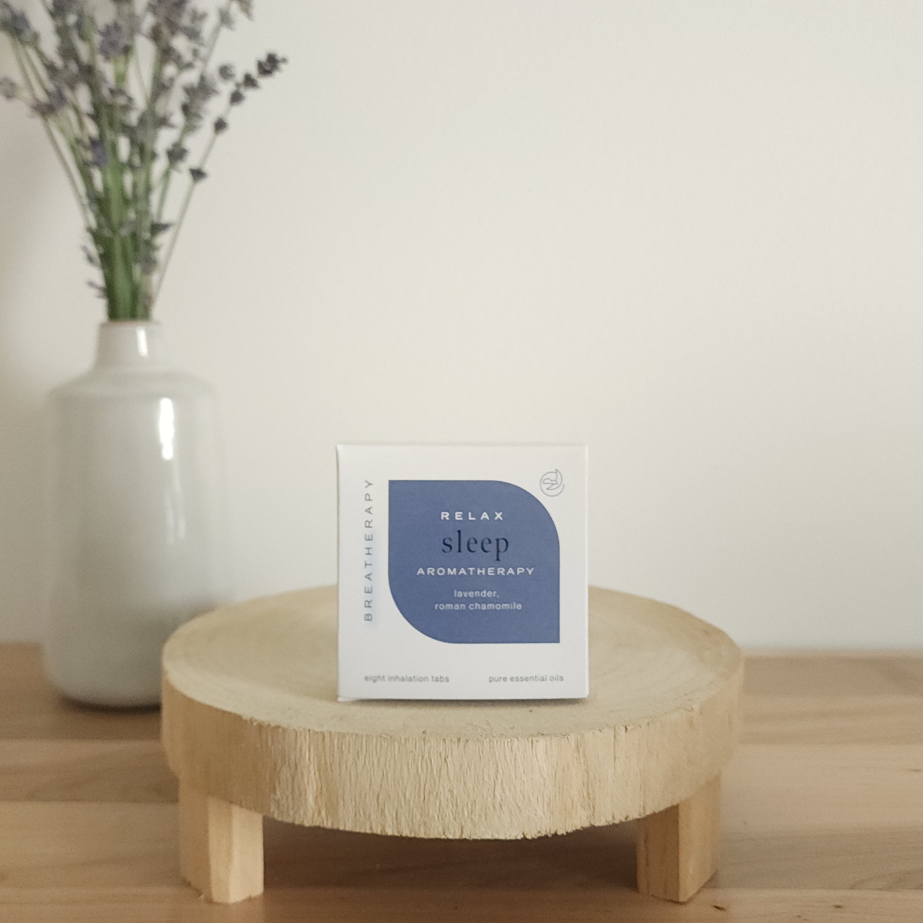 RELAX sleep aromatherapy patches package with dark blue label displayed on a round wooden stand next to a white ceramic vase with dried lavender stems