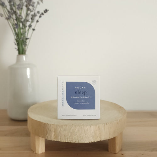 RELAX sleep aromatherapy patches package with dark blue label displayed on a round wooden stand next to a white ceramic vase with dried lavender stems