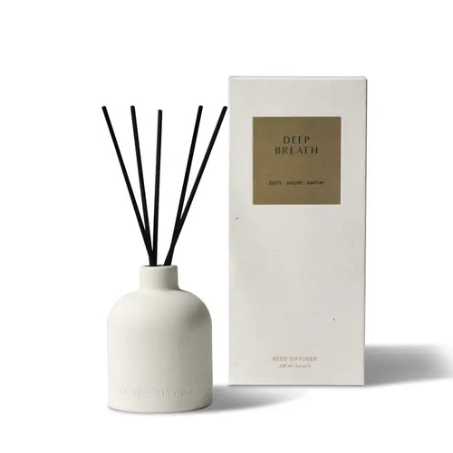 White ceramic diffuser bottle with black reeds, labeled 'DEEP BREATH' and 'ZESTY WOODY EARTHY', next to a white box labeled 'DEEP BREATH' and 'REED DIFFUSER'.