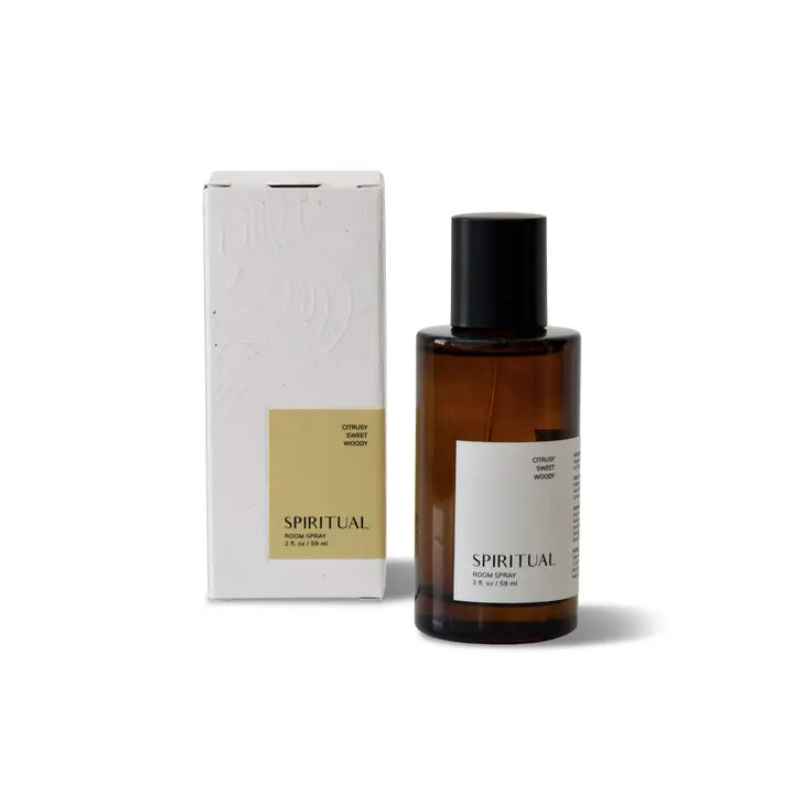 Brown glass bottle of Spiritual Room Spray standing next to its white cardboard box packaging. The bottle and box both feature labels with the text 'Spiritual Room Spray' and 'Citrusy Sweet Woody'. The bottle has a black spray nozzle and cap.