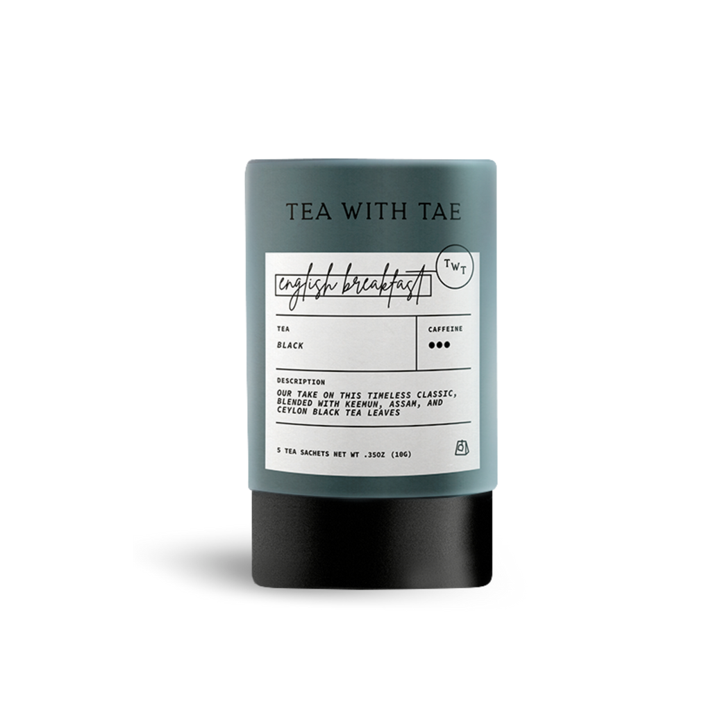 Dark gray cylindrical tea packaging labeled 'TEA WITH TAE' and 'english breakfast', with text describing 'Black' tea as 'our take on this timeless classic, blended with Kenyan, Assam, and Ceylon black tea leaves', on a white background.
