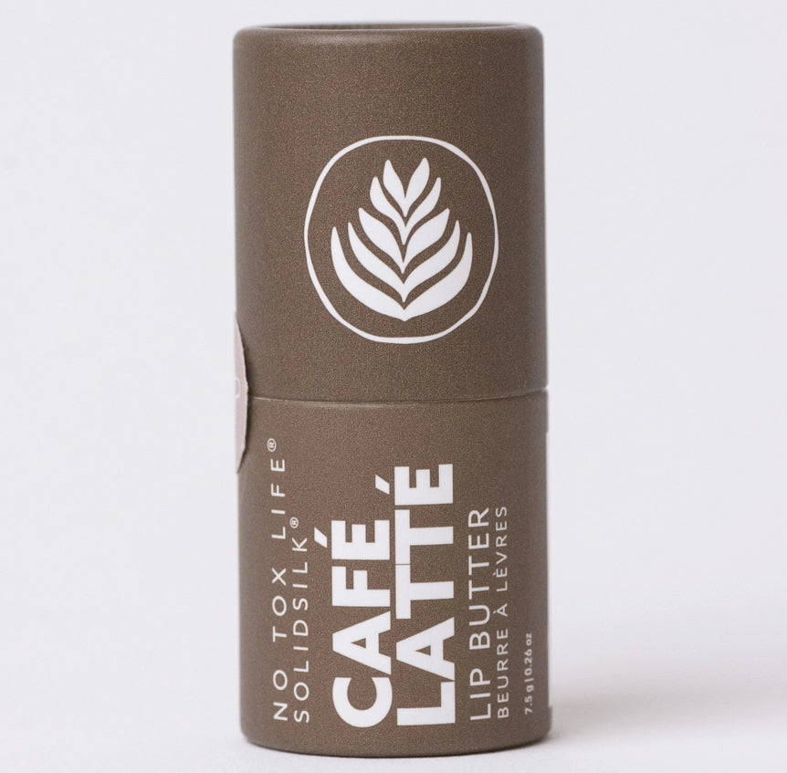 Brown paperboard tube labeled 'NO TOX LIFE SOLIDSILK CAFÉ LATTÉ LIP BUTTER BEURRE À LÈVRES' with a white latte art design, standing upright on a white background.