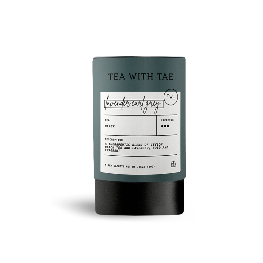 Dark gray cylindrical tea packaging labeled 'TEA WITH TAE' and 'lavender earl grey', with text describing 'Black' tea as 'a therapeutic blend of Ceylon black tea and lavender, bold and fragrant', on a white background.