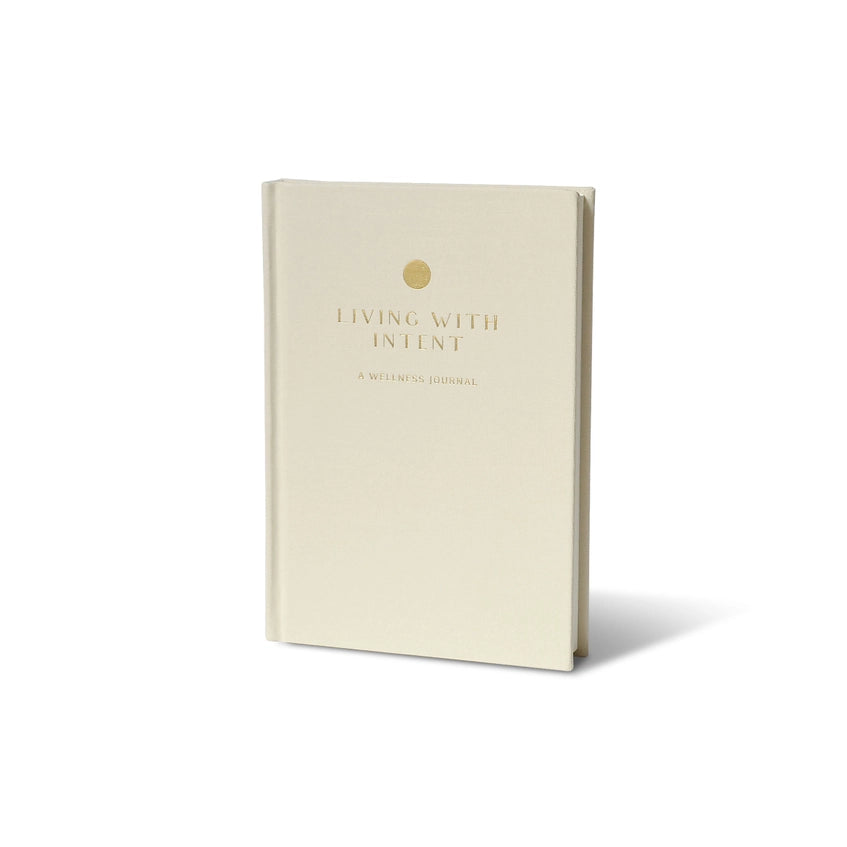 Cream-colored Wellness Journal with gold dot and text 'LIVING WITH INTENT' and 'A WELLNESS JOURNAL' on the cover, standing upright on a white background.